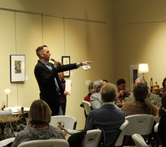 Auctioneer Murl Riedel points at a winning bidder during KMA's Live Auction as others seated at tables look on.