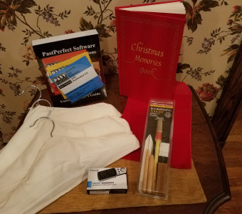 Bundle of museum items, including a copy of Past Perfect museum software, Christmas Memories book, bookbinding kit, and covered hangers for Live Auction