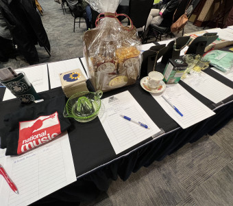 Silent auction table with shirts, glassware, gift baskets, tea, jewelry, books and more, plus bid sheets.