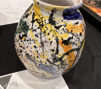 Large ceramic vase with a light gray background and splatters of yellow, orange, green, blue and black covering it.