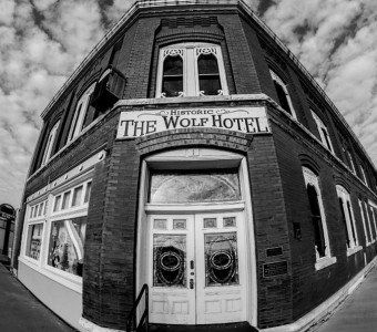 Black and white fish eye image of the 2 story brick Historic Wolf hotel with white and glass double doors inset in the corner.