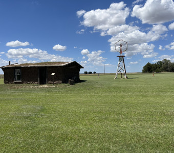 Image of building and windmill on green grass with blue skies and puffy white clouds overhead at the Santa Fe Trail Center Museum & Research Library.