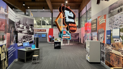A neon sign for the "White Haven Motor Lodge" sits in the middle of an exhibit space with photos, text, and artifacts around it.