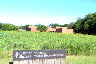 Exterior of the red brick Kauffman Museum with a green prairie and sign reading "Kauffman Museum Tallgrass Prairie Reconstruction" in front.