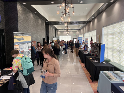 A long hotel hallway is filled with people and exhibit tables on both sides.