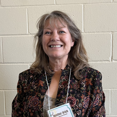 Image of Heather Urich wearing a floral jacket and a nametag on a lanyard.