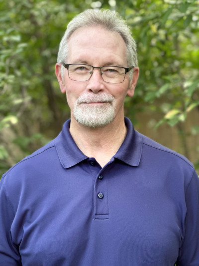Image of James Locklear, a man with grayish white hair and beard, wearing glasses and a dark blue polo shirt.