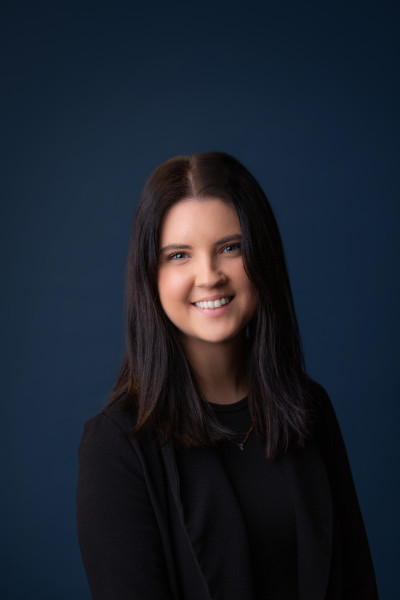 Image of Hannah Crickman with long, dark brown hair and a black shirt in front of a dark blue backdrop.