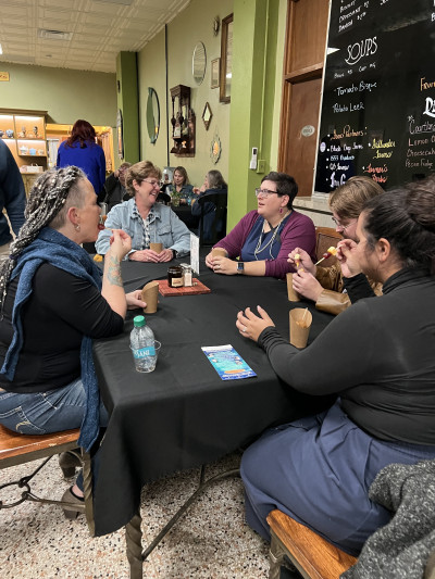 Image of KMA conference attendees sitting around a square table with decorated green walls and a blackboard menu behind them.