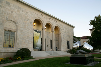 Image of a stone building taken from the left side with two columns connected by arches and "Mulvane Art Museum" at the top with a silver sculpture in front