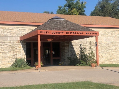 Exterior of the stone building with a covered entryway with the words "Riley County Historical Museum" at the top.