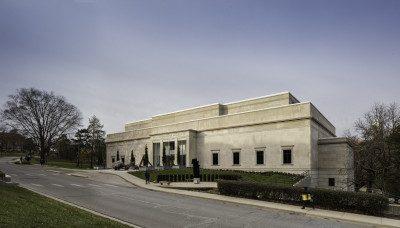 Image of the stone Spencer Museum of Art taken off-center from the right as you face the building with blue sky overhead and a road in front.