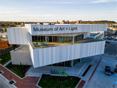 External image of the Museum of Art + Light from roof level featuring walls of windows, an outdoor terrace, and the entrance with "MoA+L" letters.
