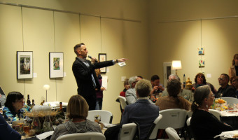 Auctioneer Murl Riedel points at a winning bidder during KMA's Live Auction as others seated at tables look on.