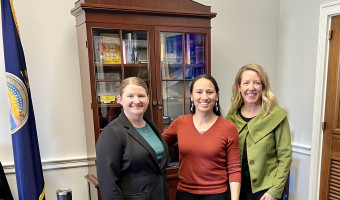 KMA Assistant Director Jamin Landavazo, Kansas Representative Sharice Davids, and KMA member and President/CEO of Kansas Children's Discovery Center Dené Mosier stand in front of a cabinet and Kansas flag in Rep. David's Washington office.