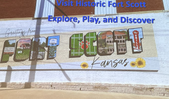 A postcard-style mural says "Greetings from Fort Scott Kansas" with pictures inside the letters that spell out "Fort Scott."  The photo of the mural is overlayed with text: "Visit Historic Fort Scott - Explore, Play and Discover