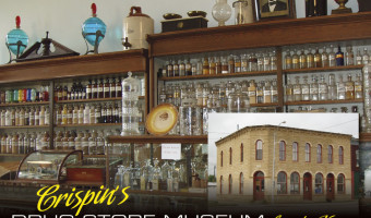 An image of two wooden cabinets and a counter display case holding glass medicine bottles.  An imposed photo of the exterior of a post-rock building with arched doors and windows.  Text at the bottom says "Crispin's Drug Store Museum, Lincoln, Kansas"