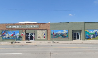 Exterior of the brick Meade Historical Museum, with painted murals and flags in front