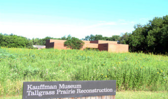 Exterior of the red brick Kauffman Museum with a green prairie and sign reading "Kauffman Museum Tallgrass Prairie Reconstruction" in front.