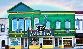 Exterior of the kelly green Oz Museum building with yellow highlights and a rainbow overhead