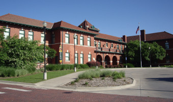 Exterior of the two-story red brick former train depot that houses the Martin and Osa Johnson Safari Museum with three visible arched doorwarys on the bottom floor.