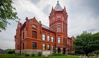 Image from the left of the two storey red brick Marshall County Historic Courthouse Museum with a tower in the middle and columns surrounding the entrance