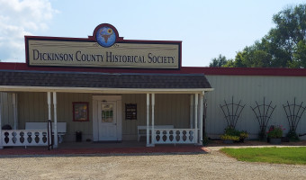 The front of the Dickinson County Historical Society, with a porch roof supported by columns and a sign with "Dickinson County Historical Socity" and a crest of a bison skull and a sunflower above.