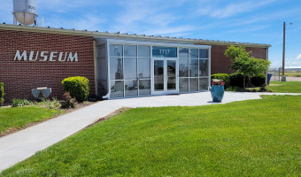 Exterior of the red brick and glass fronted High Plains Museum with green grass and blue skies.