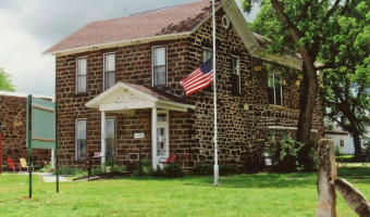 Image of the two story brick Ellsworth County Historical Society with a white portico over the door and a flag at half staff in front.