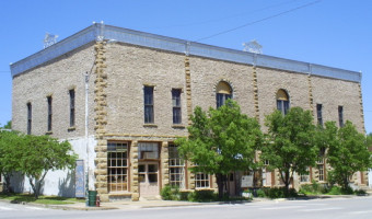 Exterior of the two story limestone Emmett Kelly Museum with the blue awning entrance flanked by trees.