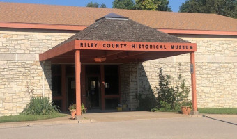 Exterior of the stone building with a covered entryway with the words "Riley County Historical Museum" at the top.
