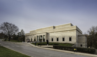 Image of the stone Spencer Museum of Art taken off-center from the right as you face the building with blue sky overhead and a road in front.