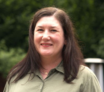Image of Shannon Hsu smiling wearing a sage green collared button up shirt with dark hair past her shoulders.