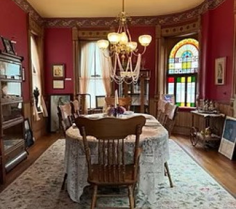 Interior dining room with of the Amelia Earhart Birthplace Museum with stained glass windows, a chandalier, and dining table with tablecloth and chairs.