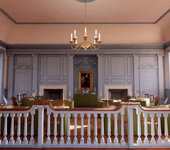 Image of a light blue room at Benedictine College with paneling, a chandelier, and desks with railing in the foreground that serves as a replica of the Assembly Room where the Declaration of Independence was debated and signed.