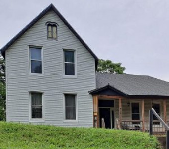 Image of the Dilgert House in Atchison, a two storey gray house with a one storey addition with porch 