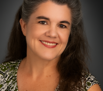 Image of Heather Dunlap, a woman with dark brown graying hair wearing a green, white, and black print shirt.