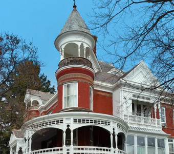 Image of red mansion with white trim and circular wrap porch beneath turret housing the Muchnic Art Gallery