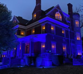 Nighttime photo of the Ravenhearse House in Atchison, a three storey mansion with candles glowing from each window.