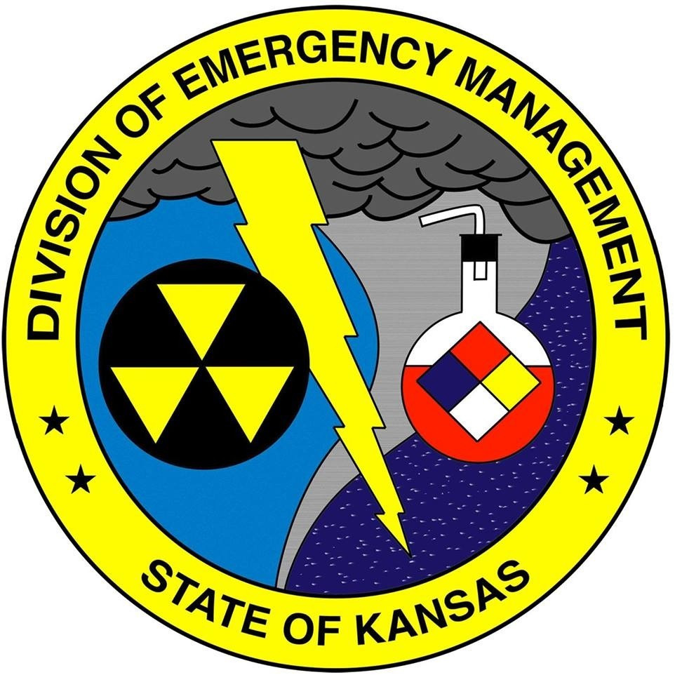 Division of Emergency Management State of Kansas logo with words around a yellow circle and inside the circle a danger sign, lightning bolt, tornado, and chemical bottle.