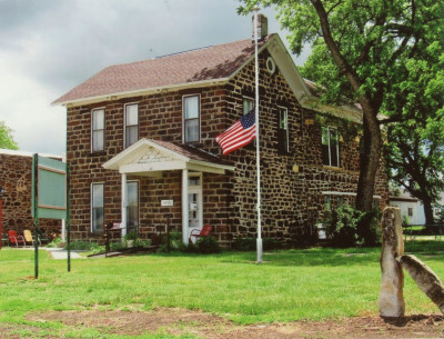 Image of the two story brick Ellsworth County Historical Society with a white portico over the door and a flag at half staff in front.