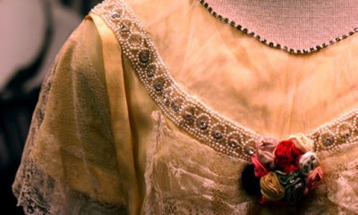 Partial image of a dress with beading, lace, and rosettes on a mannequin with black and white image behind it.