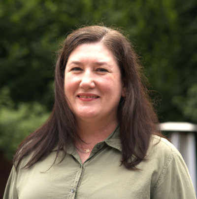 Image of Shannon Hsu smiling wearing a sage green collared button up shirt with dark hair past her shoulders.