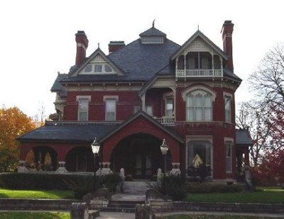 Image of a three storey red brick mansion with an arched entry and large covered wrap porch