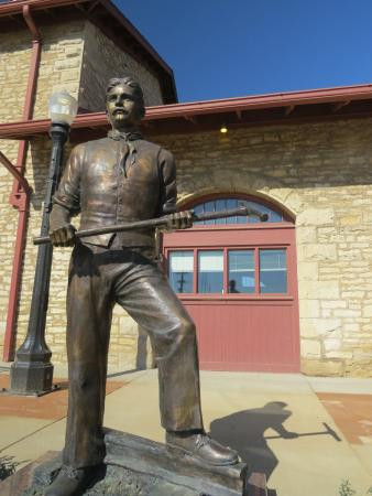 Image of railroad worker statue in front of stone building with red door topped with windows at the Atchison County Historical Society