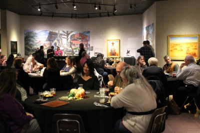 Image of people seated at tables and standing with art on the walls in the background at the Traveling Reception during the 2025 KMA Conference at Barton County Community College's Shafer Art Gallery in Great Bend.