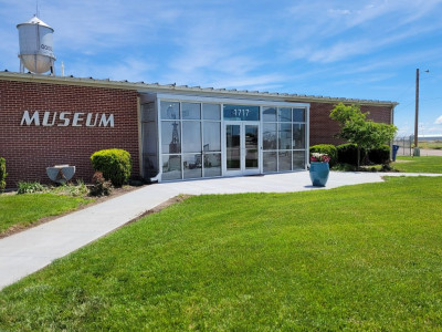 Image of the exterior of the red brick and glass High Plains Museum with a bright blue sky and clouds overhead and a green lawn in the foreground.