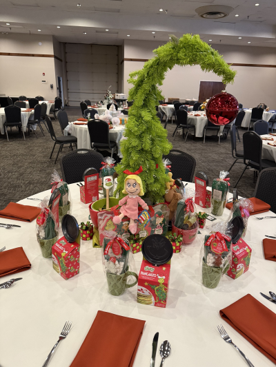 Image of Christmas tree with top bending over and red ornament hanging from it as a table centerpiece surrounded by the Grinch Who Stole Christmas items.
