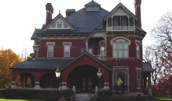 Image of a three storey red brick mansion with an arched entry and large covered wrap porch