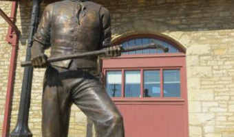 Image of railroad worker statue in front of stone building with red door topped with windows at the Atchison County Historical Society